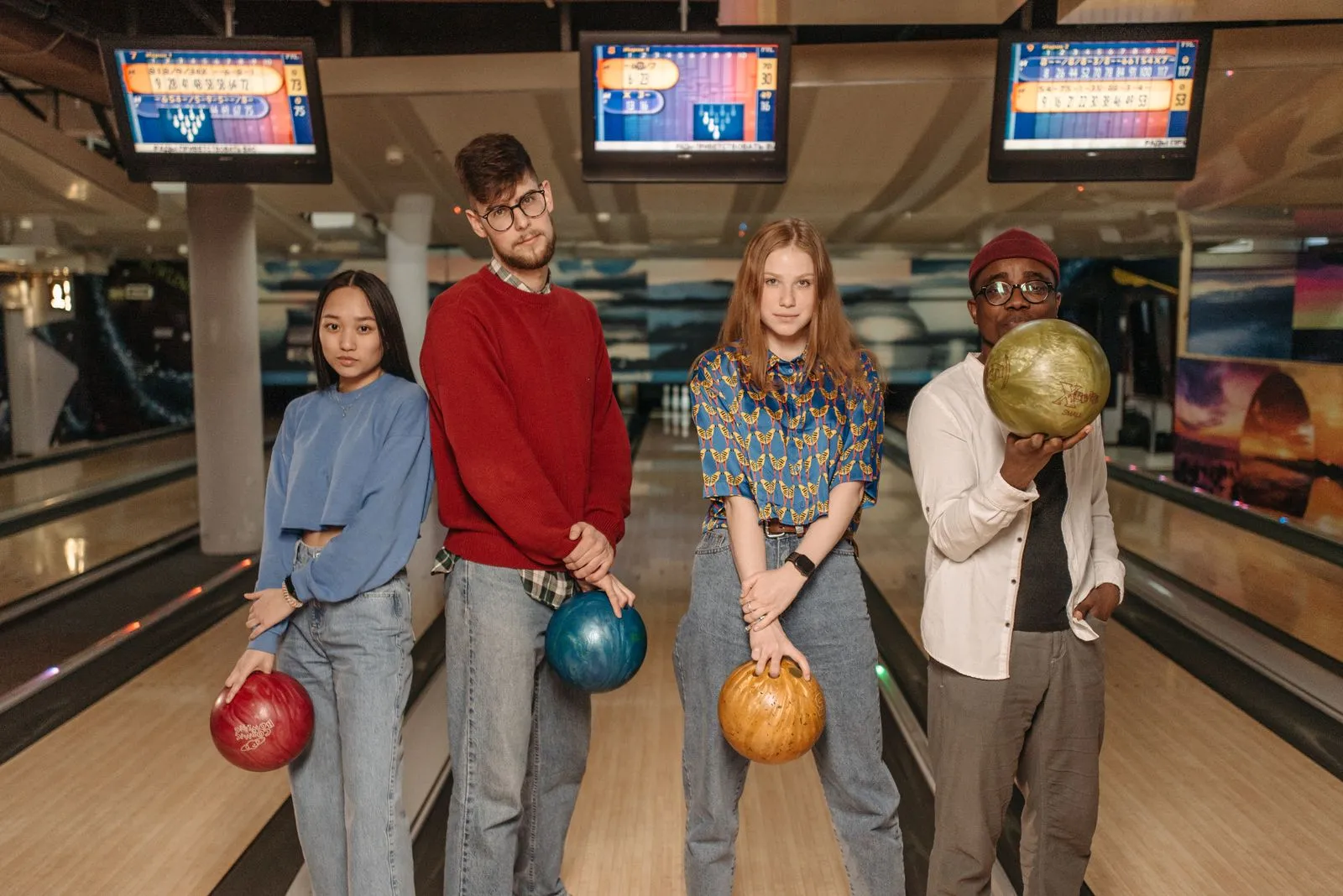 Diverse group of friends posing with bowling balls in an indoor alley.